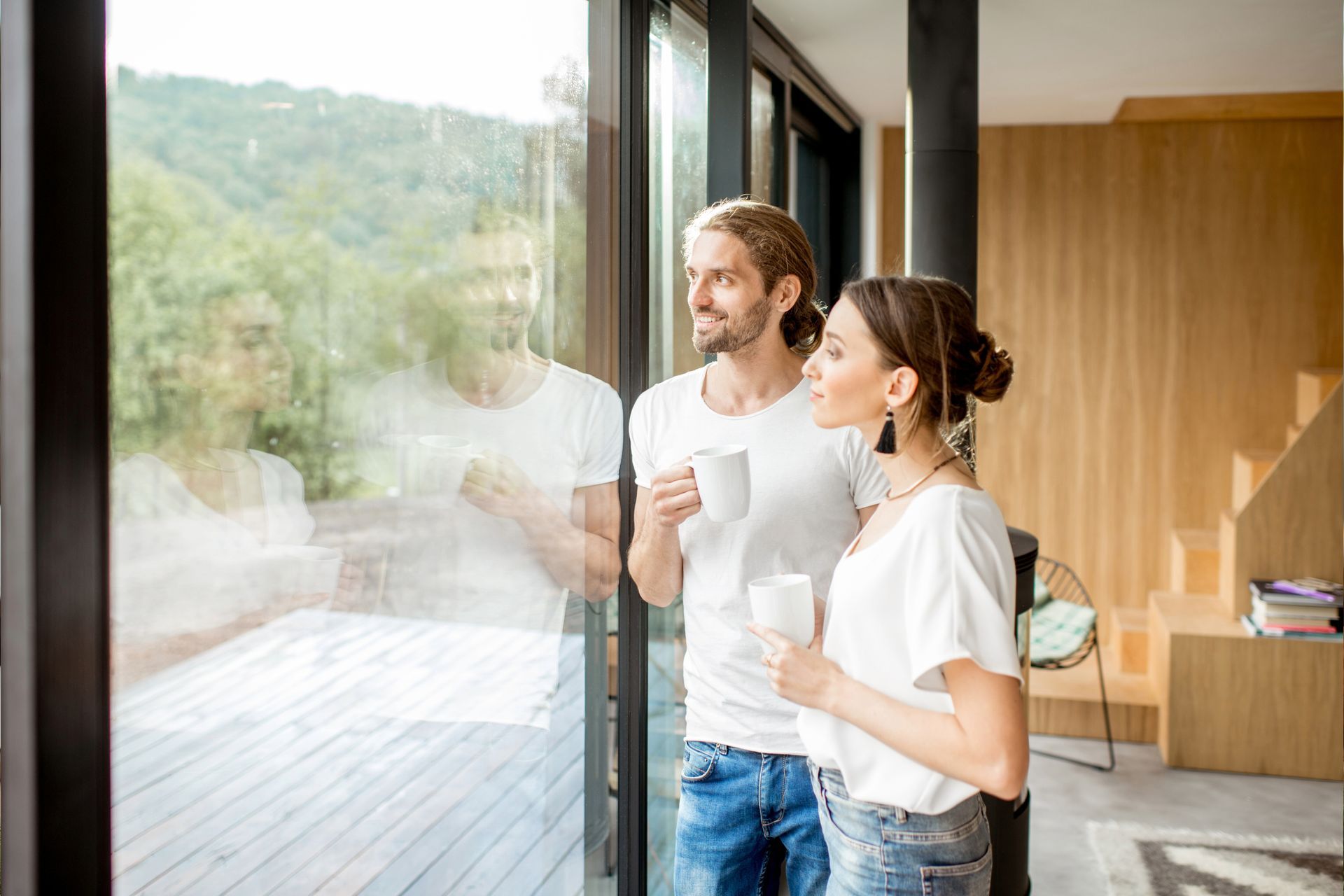 A man and a woman are drinking coffee and looking out of a window.