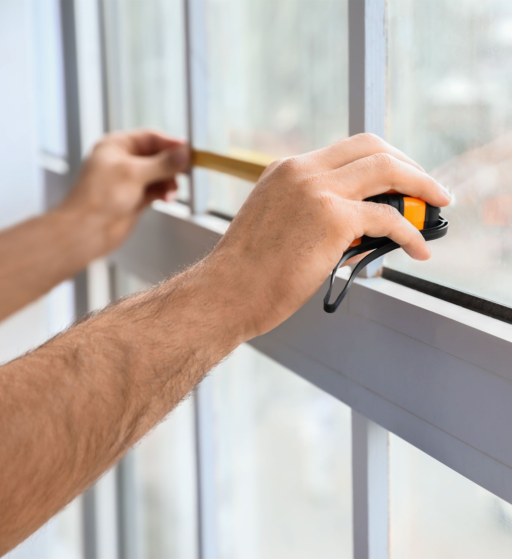 A person is measuring a window with a tape measure.