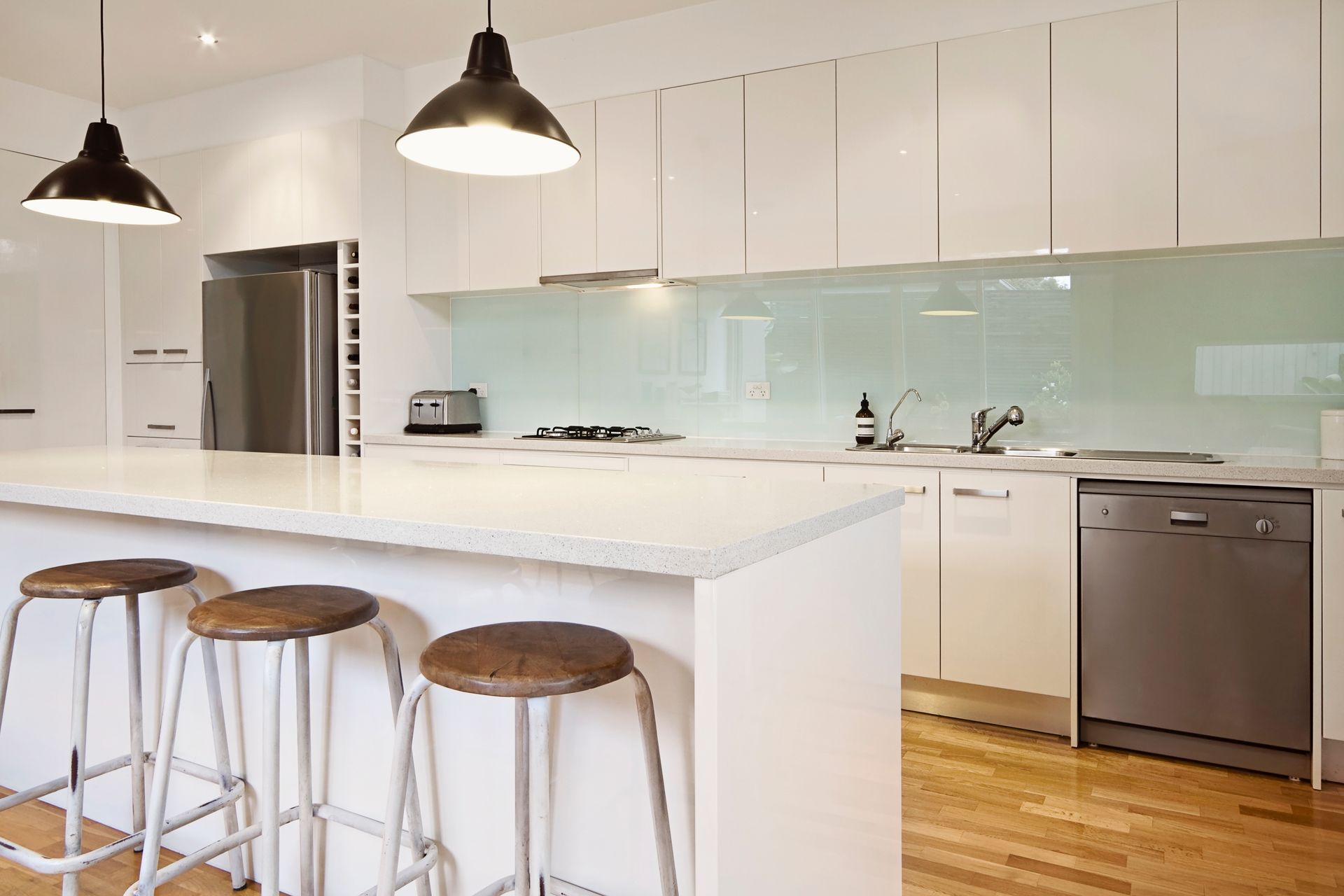 A kitchen with white cabinets , stools , a refrigerator and a dishwasher.