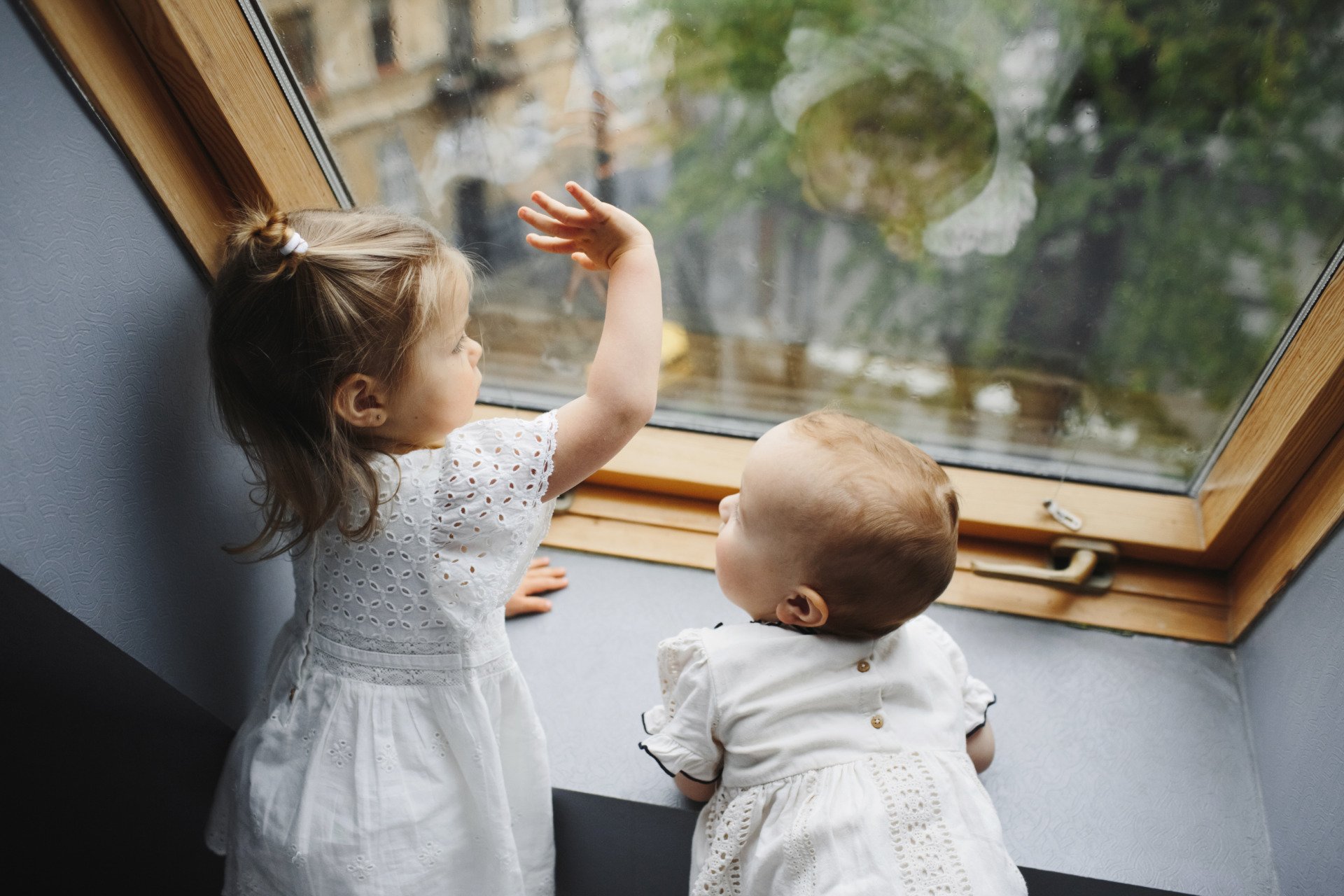 Two little girls are looking out of a window.