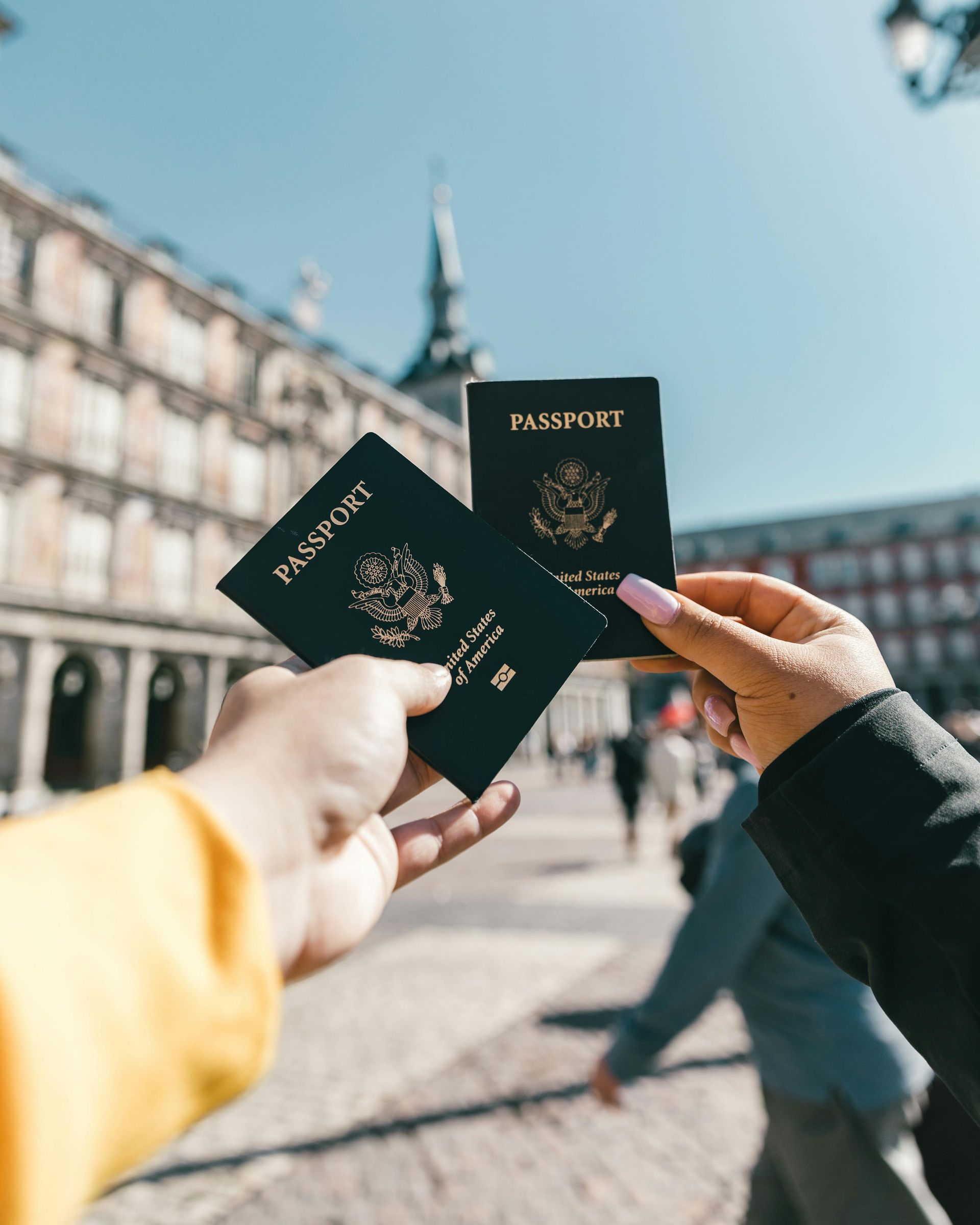 A person is holding two passports in their hands in front of a building.