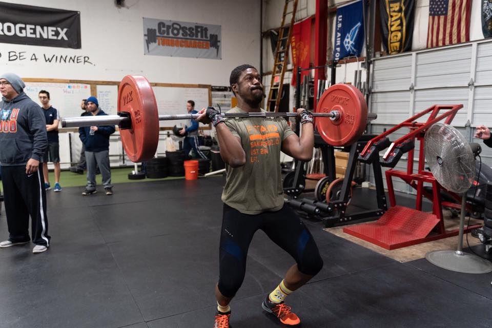 A man is squatting with a barbell at CrossFit Turbocharged gym in Cherry Hill, NJ