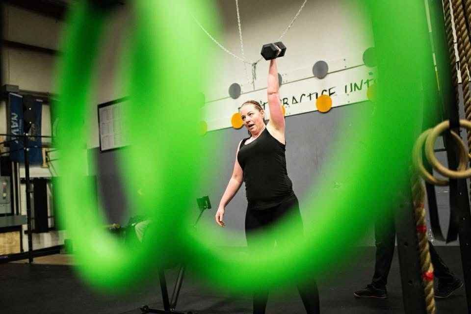 A woman is lifting a dumbbell over her head in a gym.