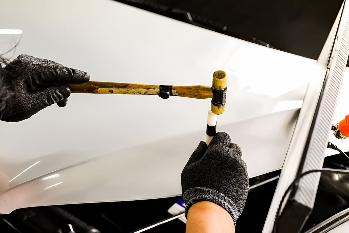 A Person Is Holding A Hammer Over A White Car — Mahers Smash Repairs in Barraba, NSW