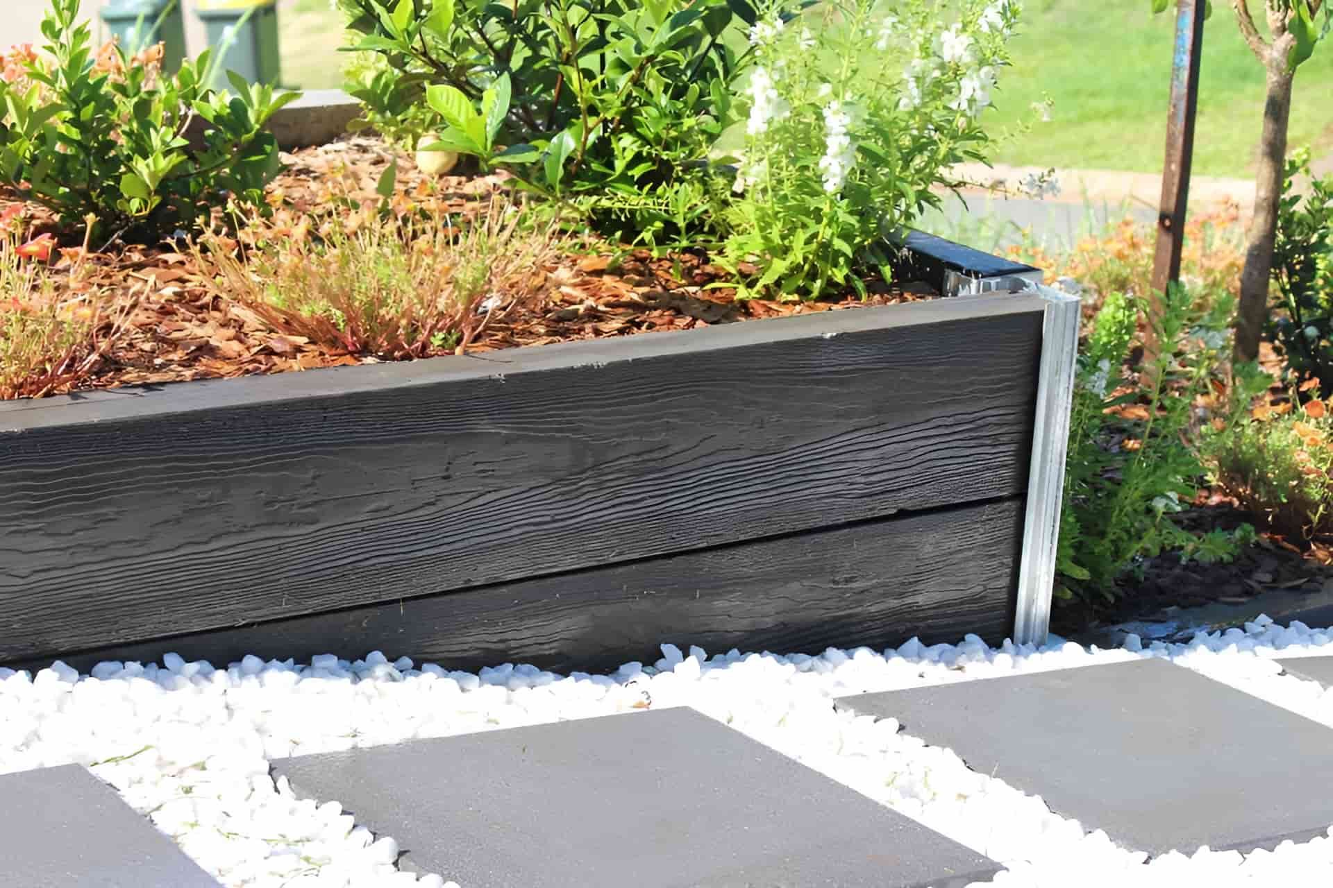 A Customized Colour Of Sleeper Filled With Plants Is Sitting Next To A Stone Walkway — NQ Prefab Concrete Products Pty Ltd In Coconuts, QLD