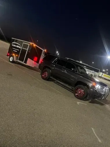 Black SUV parked beside a lit cargo trailer in a dark parking lot at night.