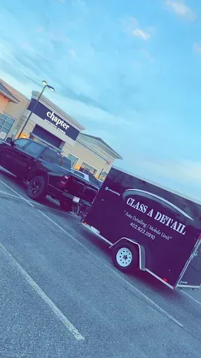 Black pickup towing a brown Cass & Bear trailer in a store parking lot under a blue sky