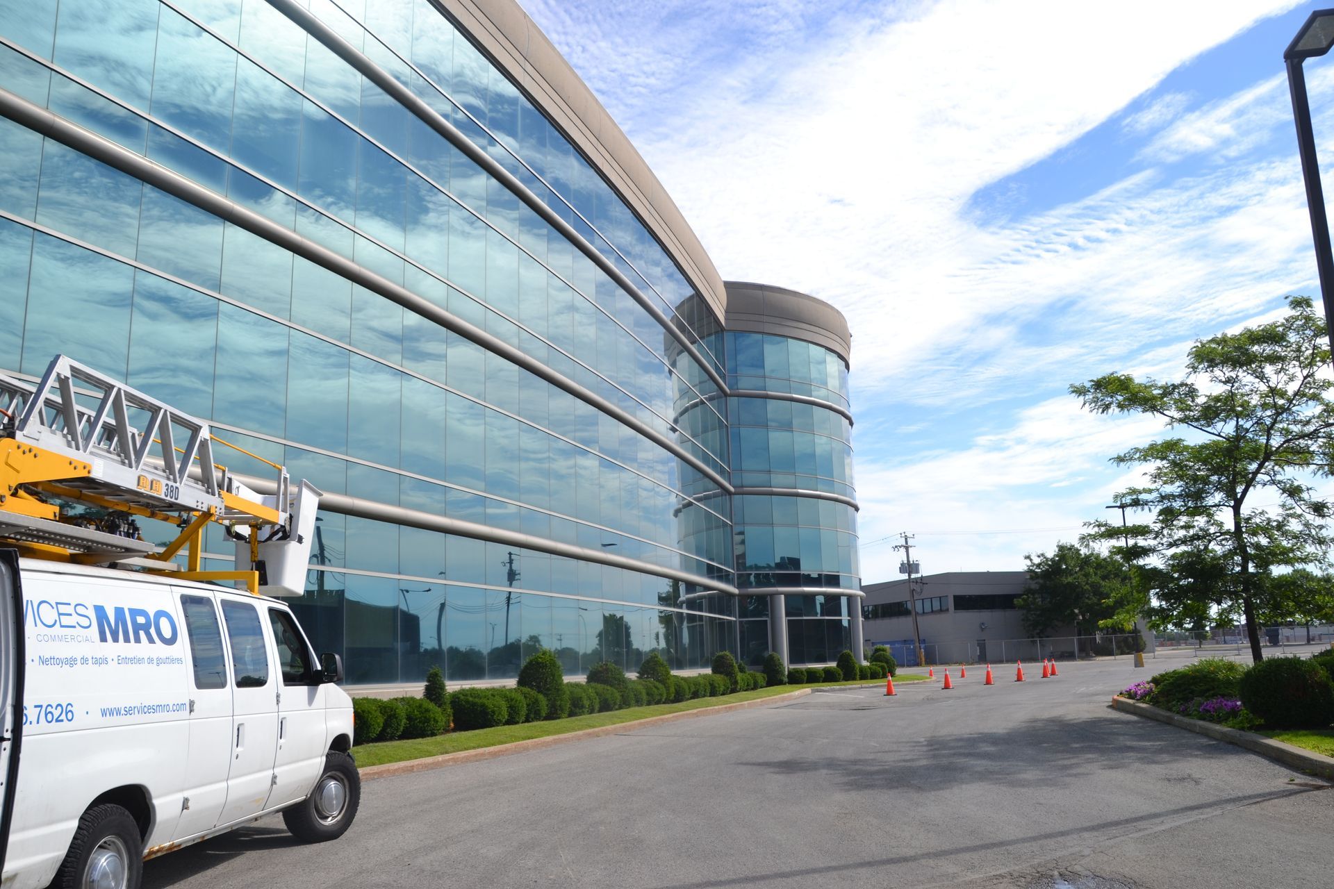 Vue extérieure d'un bâtiment moderne en verre avec une camionnette d'entretien garée dans une allée sous un ciel nuageux.