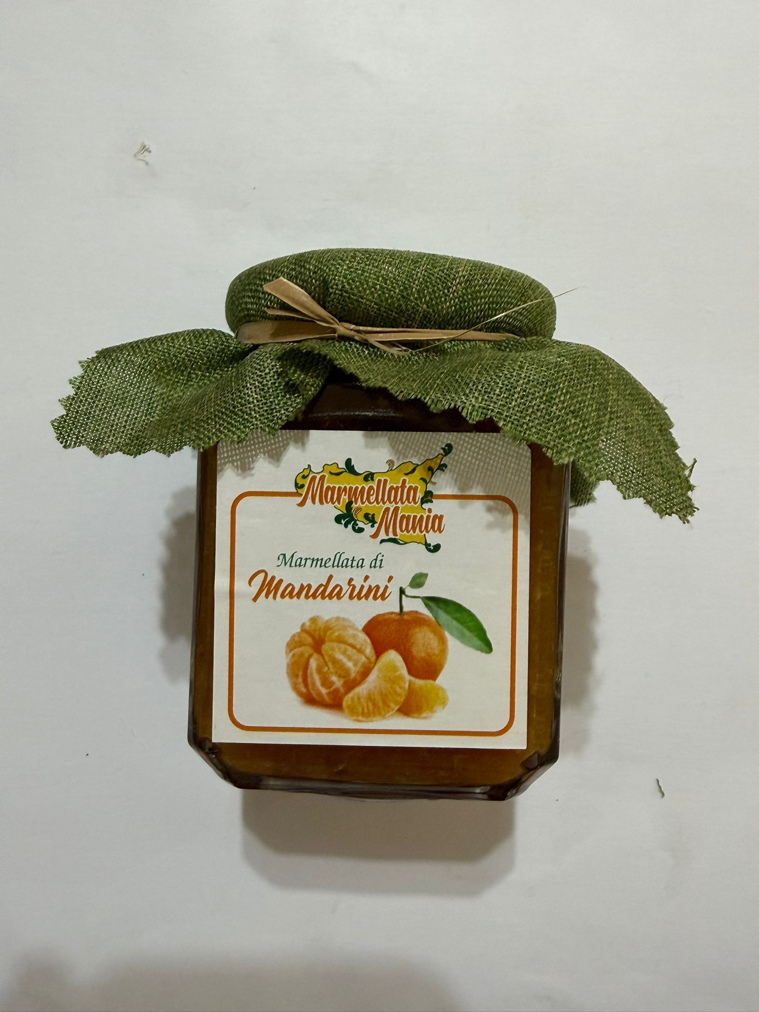 Barattolo di marmellata d'arance con foglie verdi drappeggiate sul coperchio su sfondo bianco.
