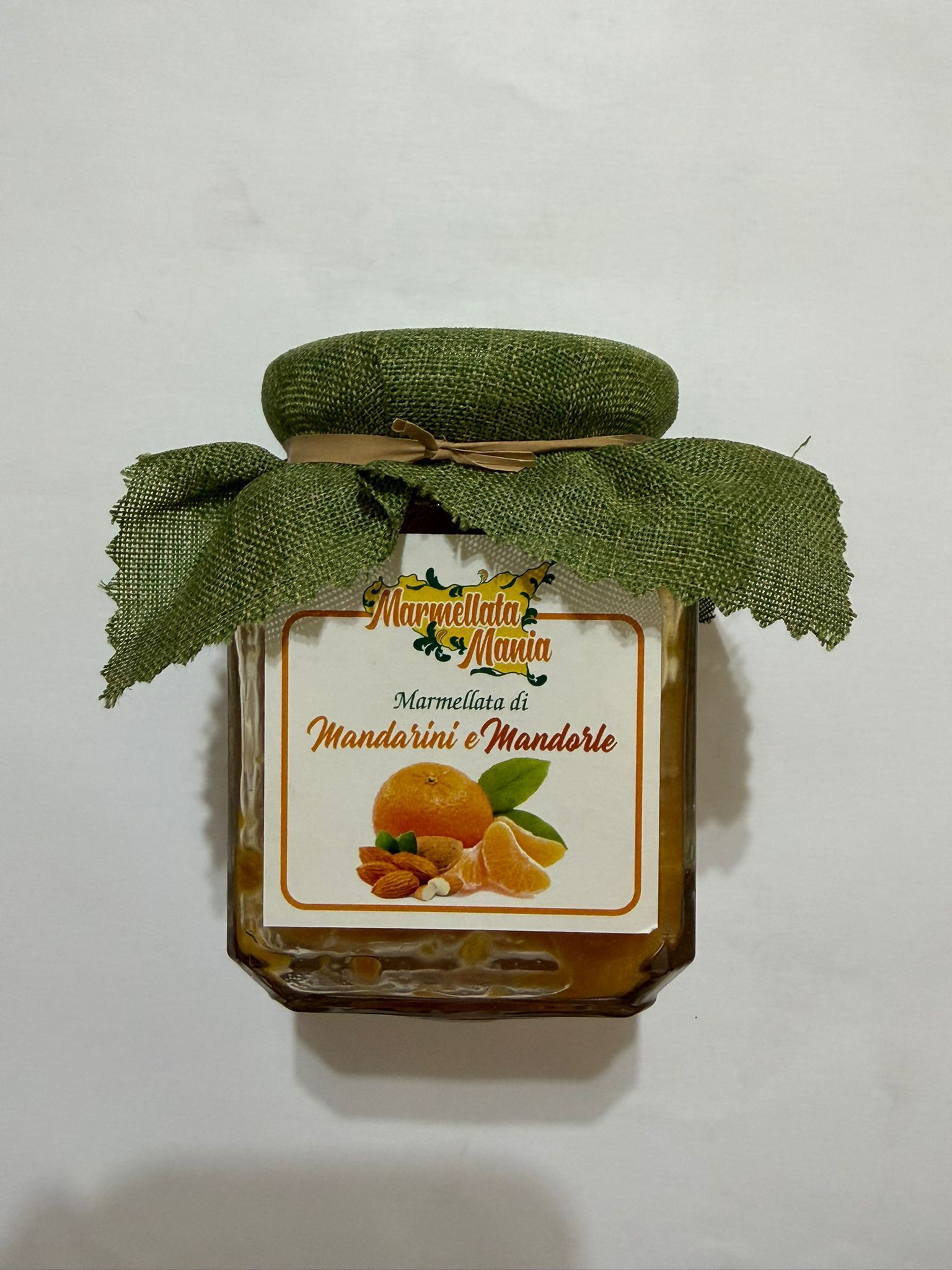 Barattolo con coperchio decorativo verde ed etichetta raffigurante della frutta, probabilmente marmellata o confettura.