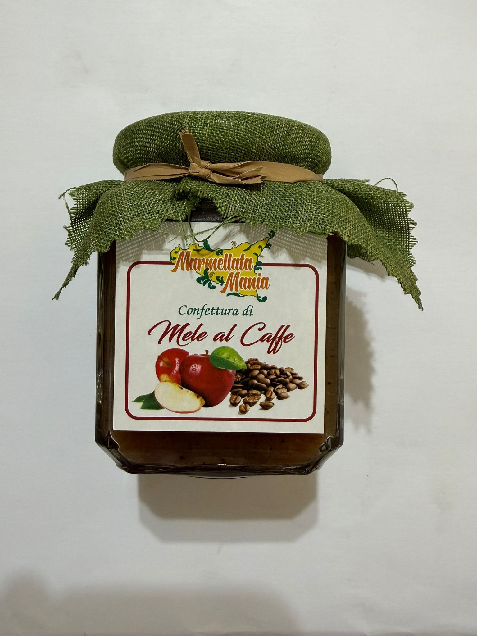 Barattolo di marmellata di caffè con coperchio in tessuto verde ed etichetta che raffigura chicchi di caffè e mele.