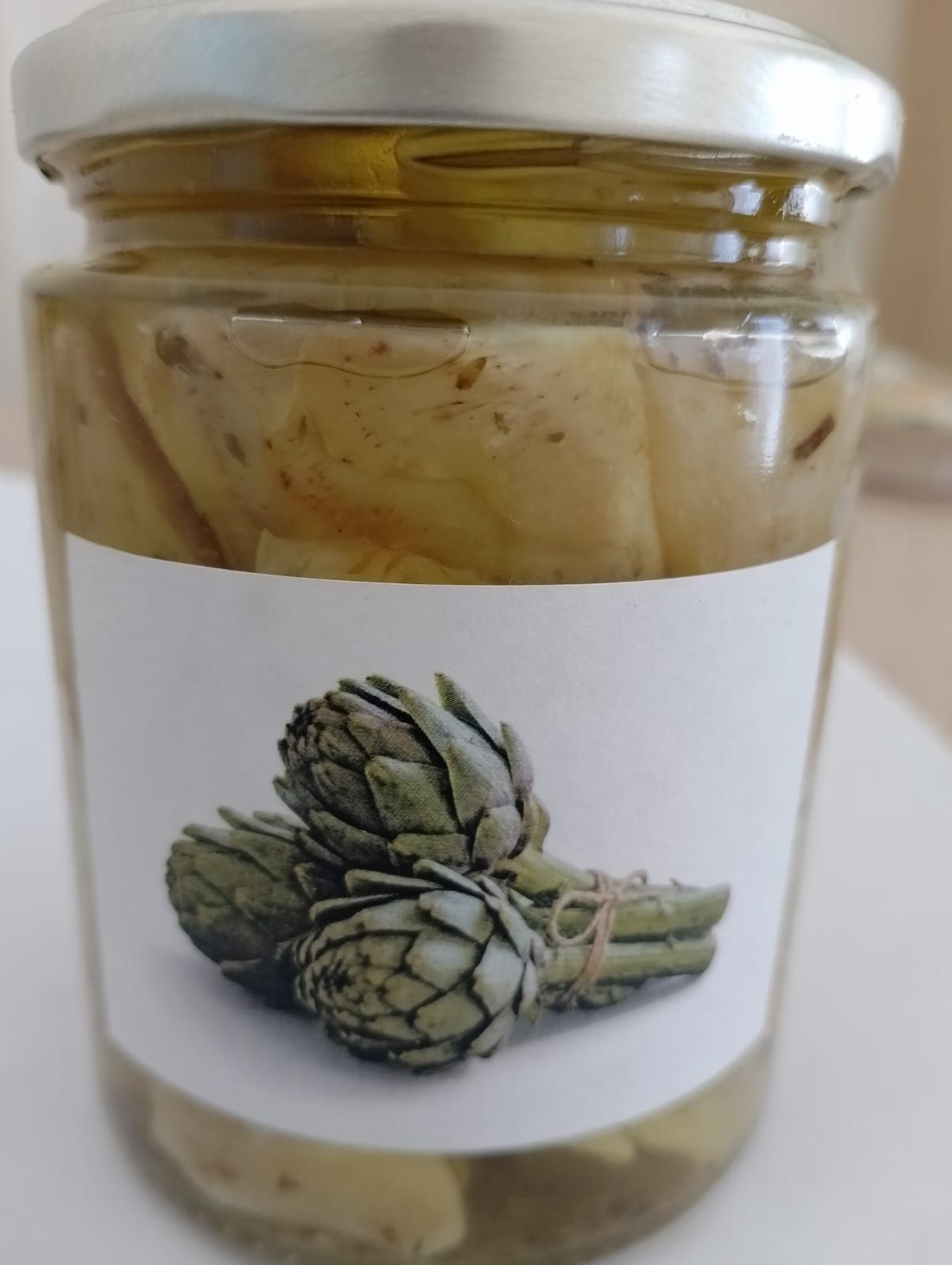 Un barattolo di vetro con coperchio argentato contenente carciofi conservati in liquido.