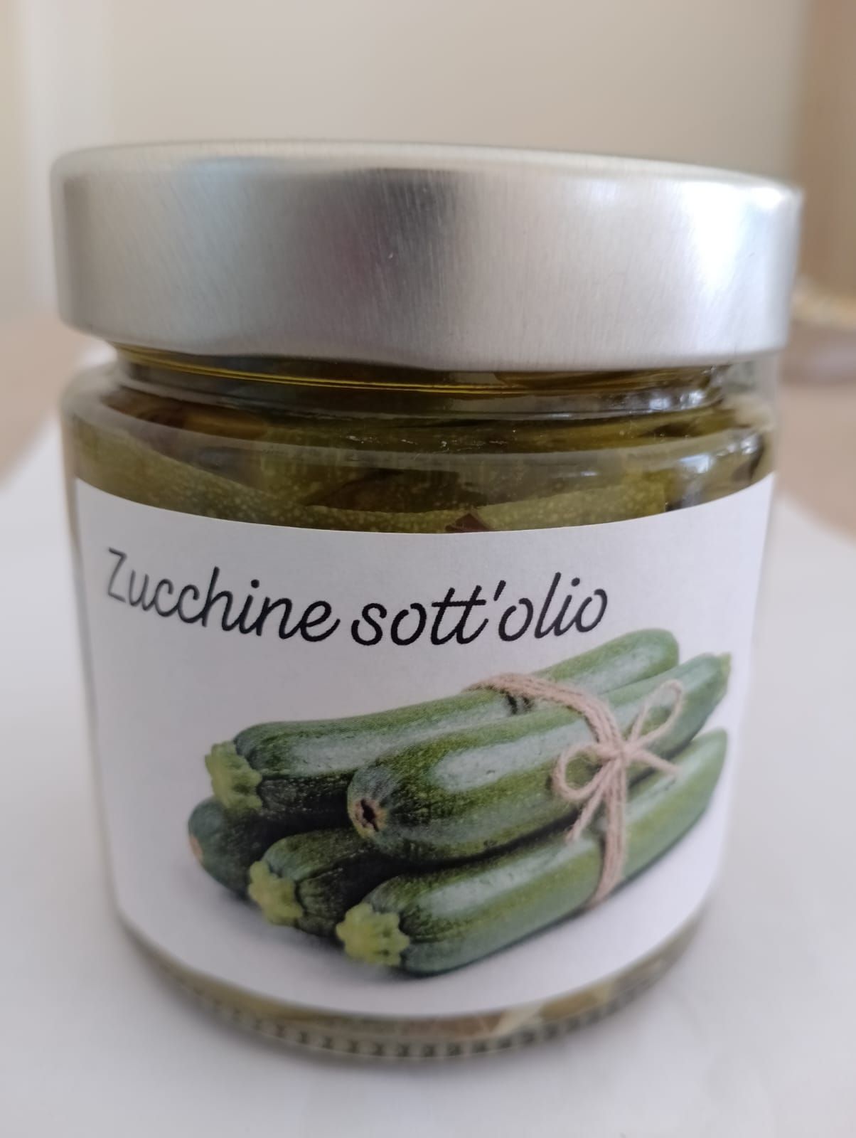 Barattolo di zucchine sott'olio con coperchio bianco ed etichetta che mostra le zucchine legate.