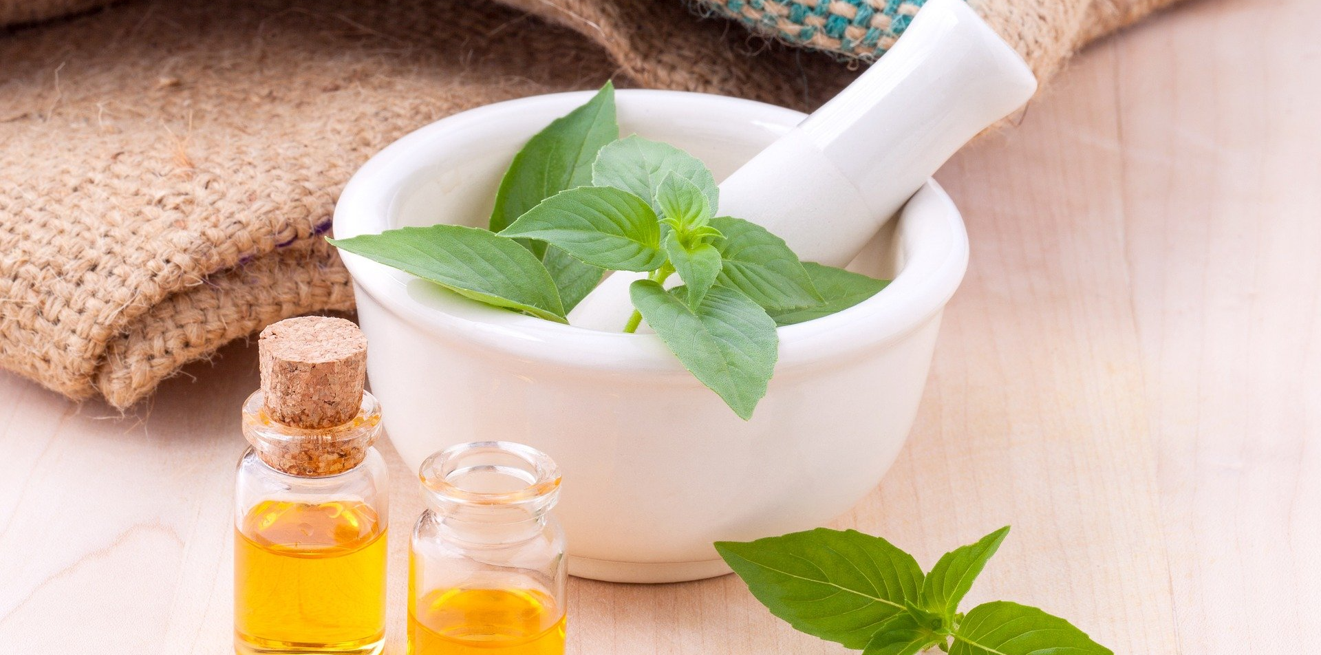 A mortar and pestle with mint leaves and two bottles of essential oil.