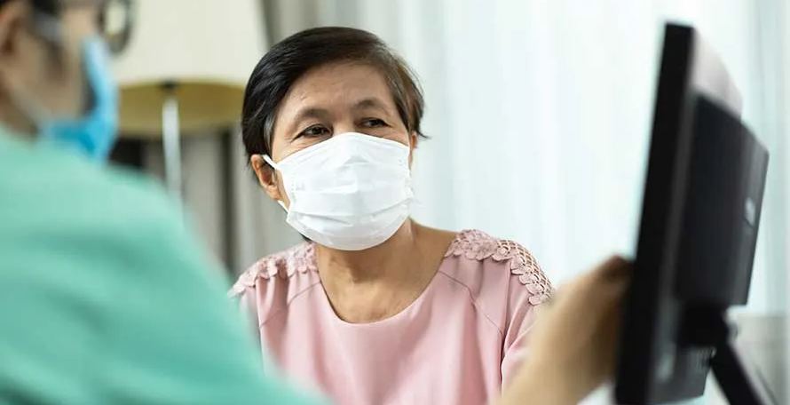 A woman wearing a mask is sitting in front of a computer monitor.