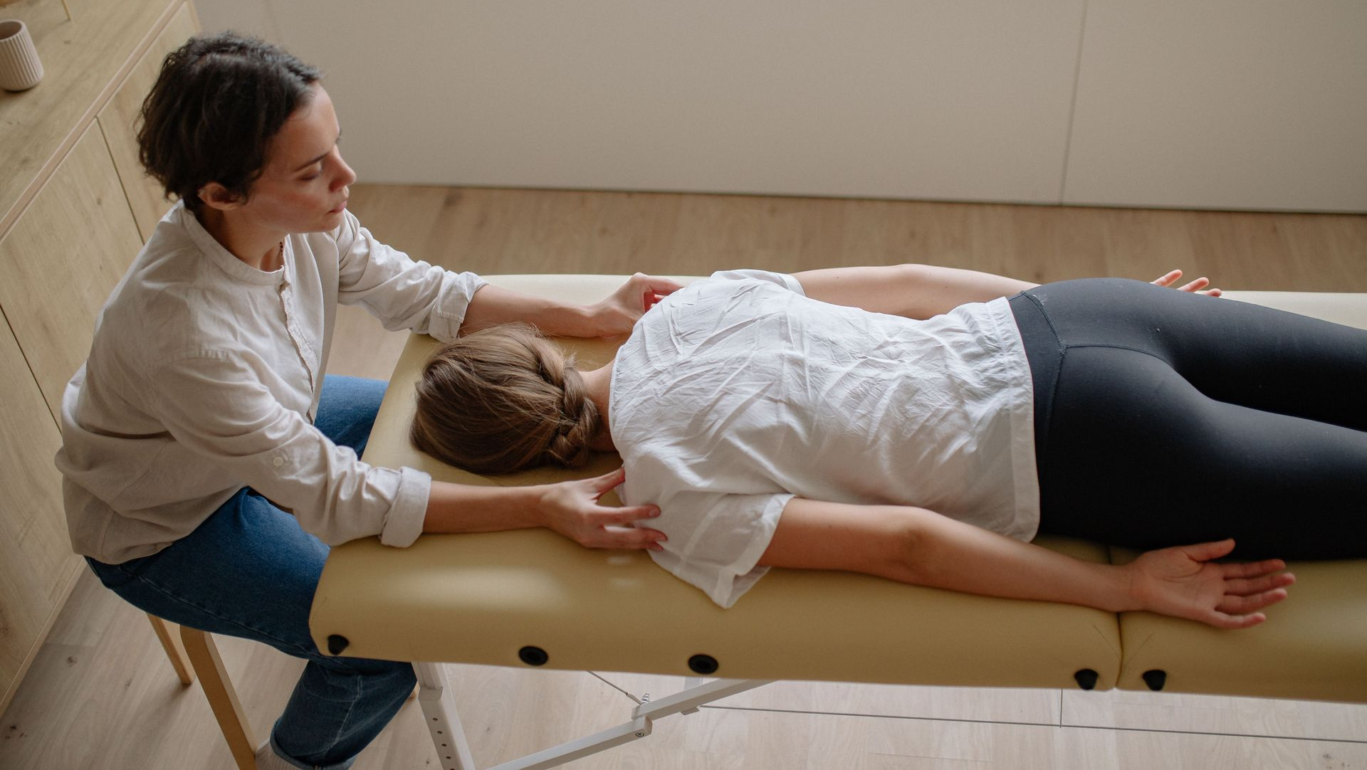 Therapist performing a massage on a person lying face down on a padded treatment table.