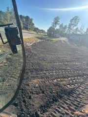 Dirt work site with tire tracks, trees in the background, visible from the inside of a vehicle.