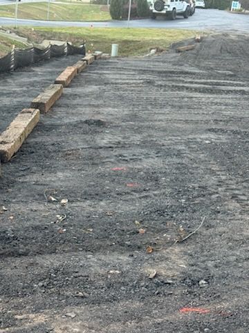 Construction site with dark gravel, wooden borders, and a vehicle in the background.
