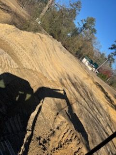 Excavated earth with tire tracks, trees, and a building in the distance.