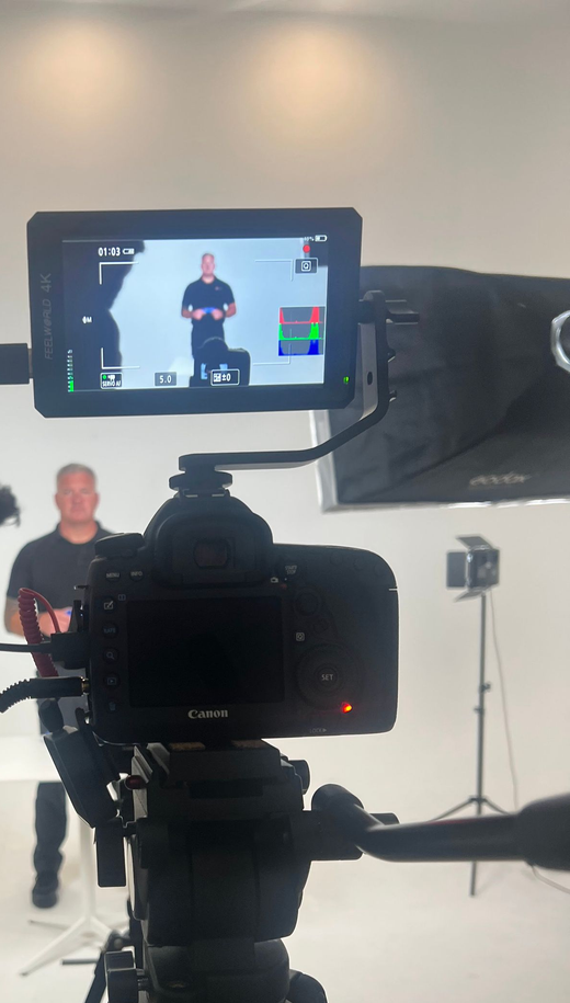 Camera setup filming a person standing in a studio, seen on an external monitor.