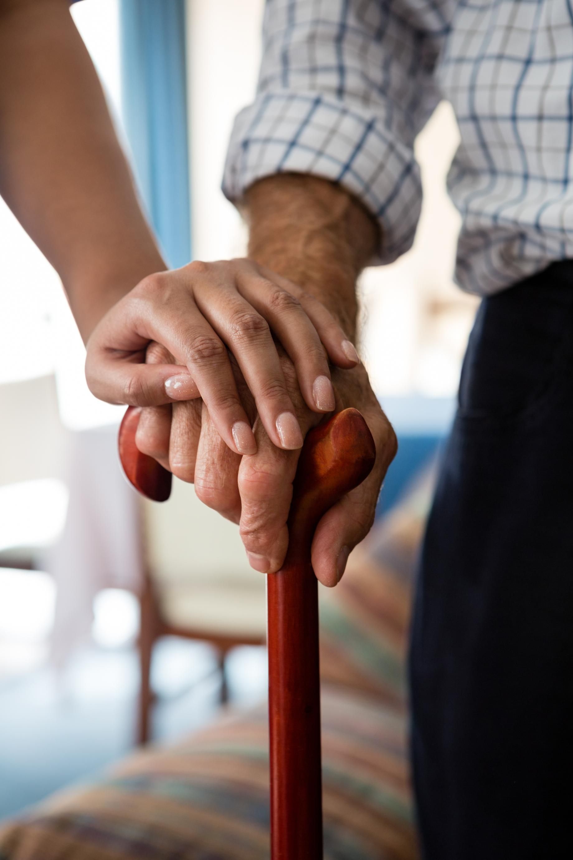 Person's hand rests on a cane, held by another person.