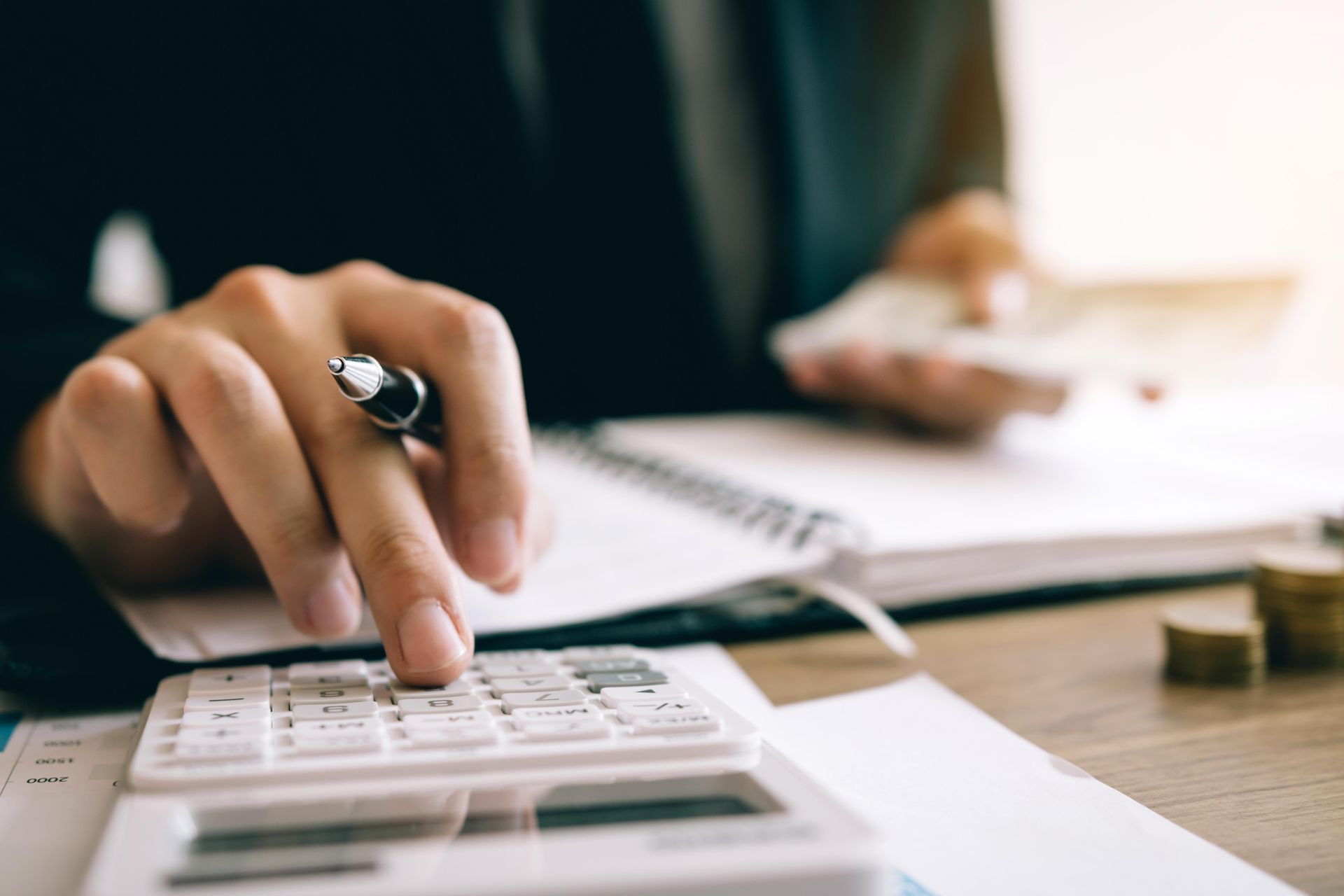 Person calculating with a calculator, pen in hand, near a notebook and money.