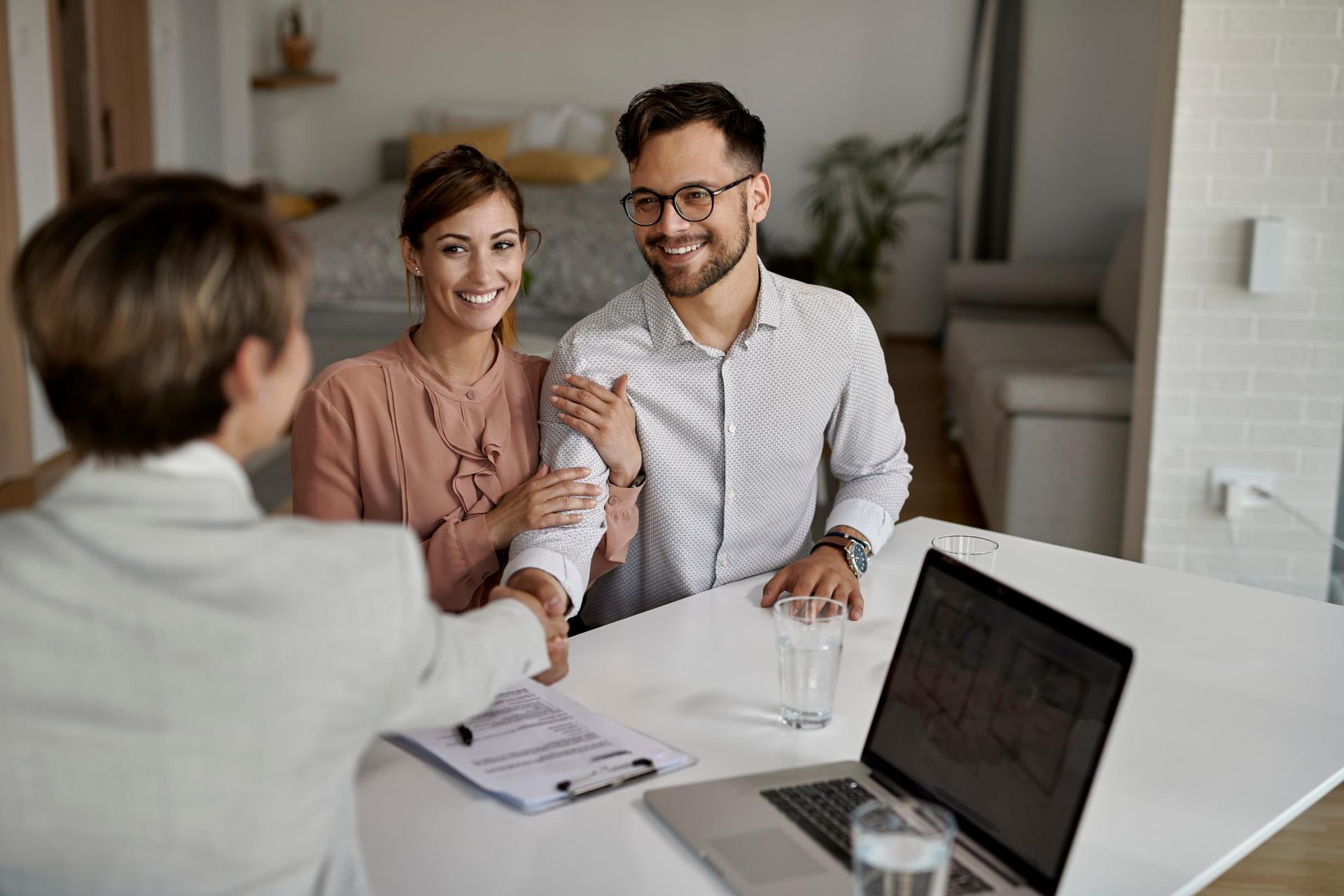 Woman shakes hands with a couple, smiling. 