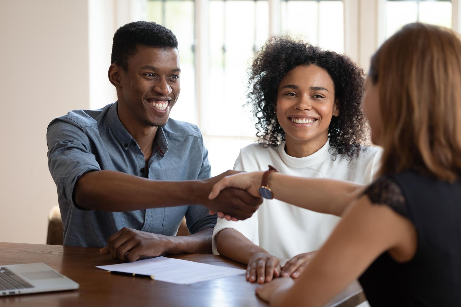 Couple shaking hands with a woman at a table, smiling, in an office setting.