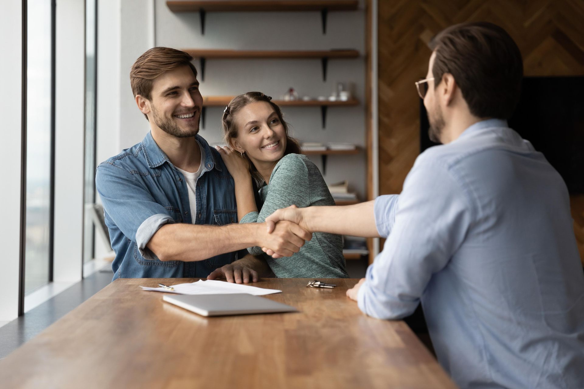 Couple shaking hands with professional at a wooden table, smiling.