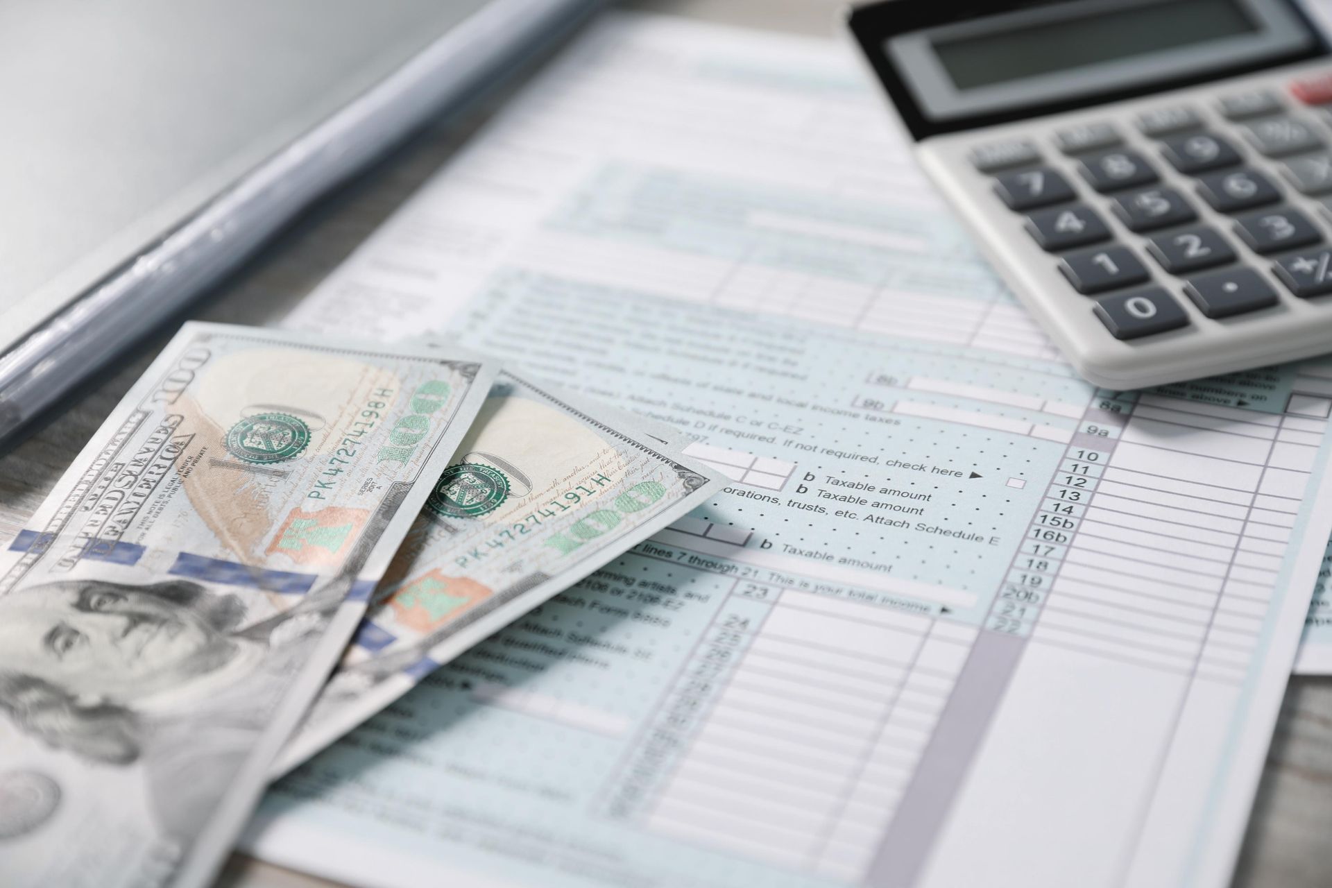 Tax forms, money, and a calculator on a desk, symbolizing financial planning and tax preparation.