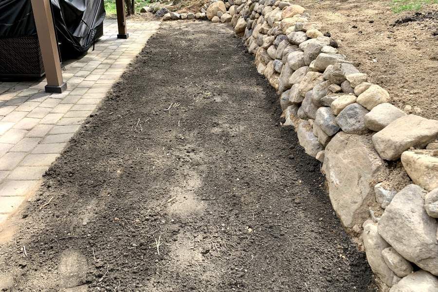 A stone wall is being built next to a brick walkway.