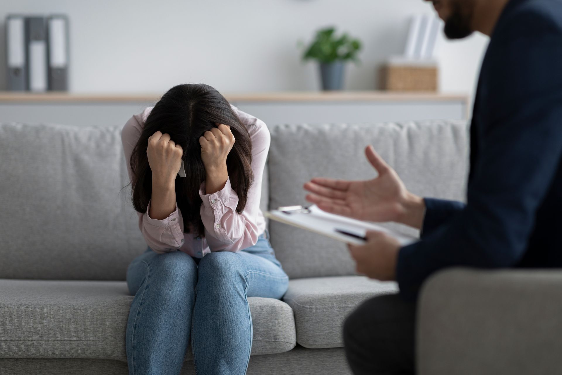 Distressed person on a couch with head in hands, facing a therapist in a counseling session