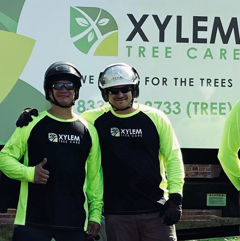 Two men are posing for a picture in front of a xylem tree care sign — Norfolk, VA — Xylem Tree Care