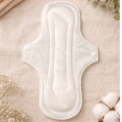 Toallas menstruales reutilizables de colores colocadas sobre una mesa con una vela y una pequeña caja de regalo.