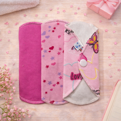 Toallas menstruales reutilizables de colores colocadas sobre una mesa con una vela y una caja de regalo.