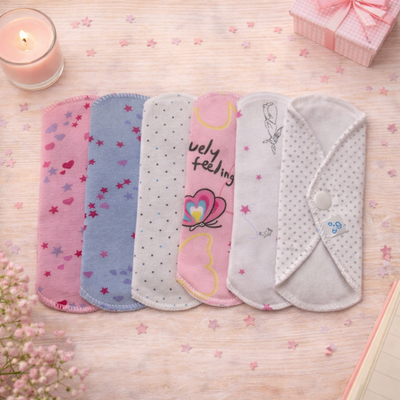 Toallas menstruales reutilizables de colores colocadas sobre una mesa con una vela y una caja de regalo.