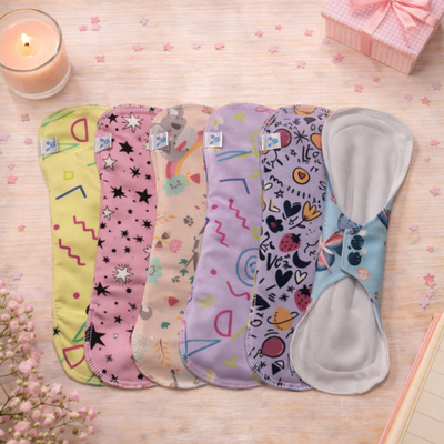 Toallas menstruales reutilizables de colores colocadas sobre una mesa con una vela y una pequeña caja de regalo.