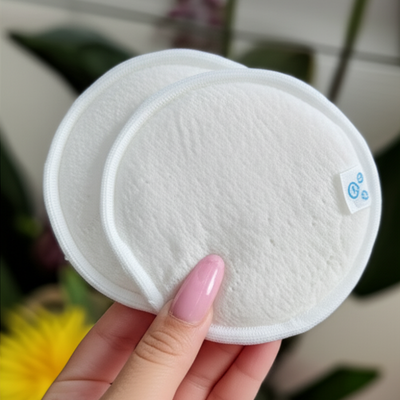 Dos discos desmaquillantes redondos, reutilizables y de color blanco, con una flor y vegetación sobre una superficie neutra.