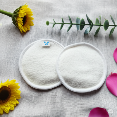 Dos discos desmaquillantes redondos, reutilizables y de color blanco, con una flor y vegetación sobre una superficie neutra.