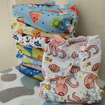 Pila de pañales de tela coloridos para bebé con patrones de frutas y temas marinos.