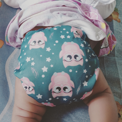 Bebé en pañal de tela verde azulado con estampado de búho y estrella.