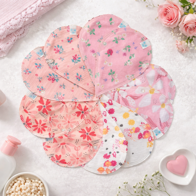 Almohadillas de lactancia florales en un arreglo de pétalos sobre una superficie blanca, con productos de baño y rosas.