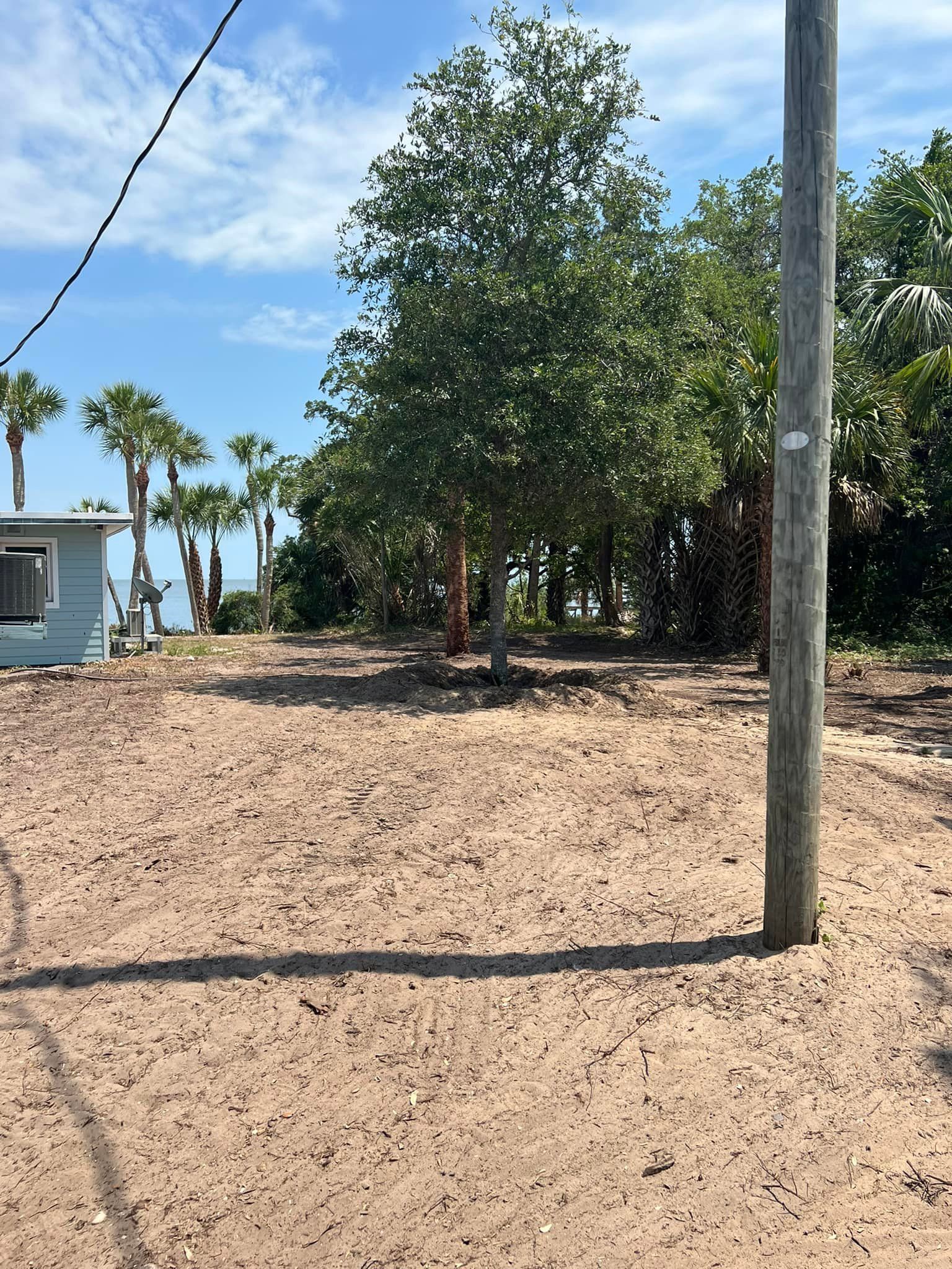 A dirt field with a house and trees in the background.
