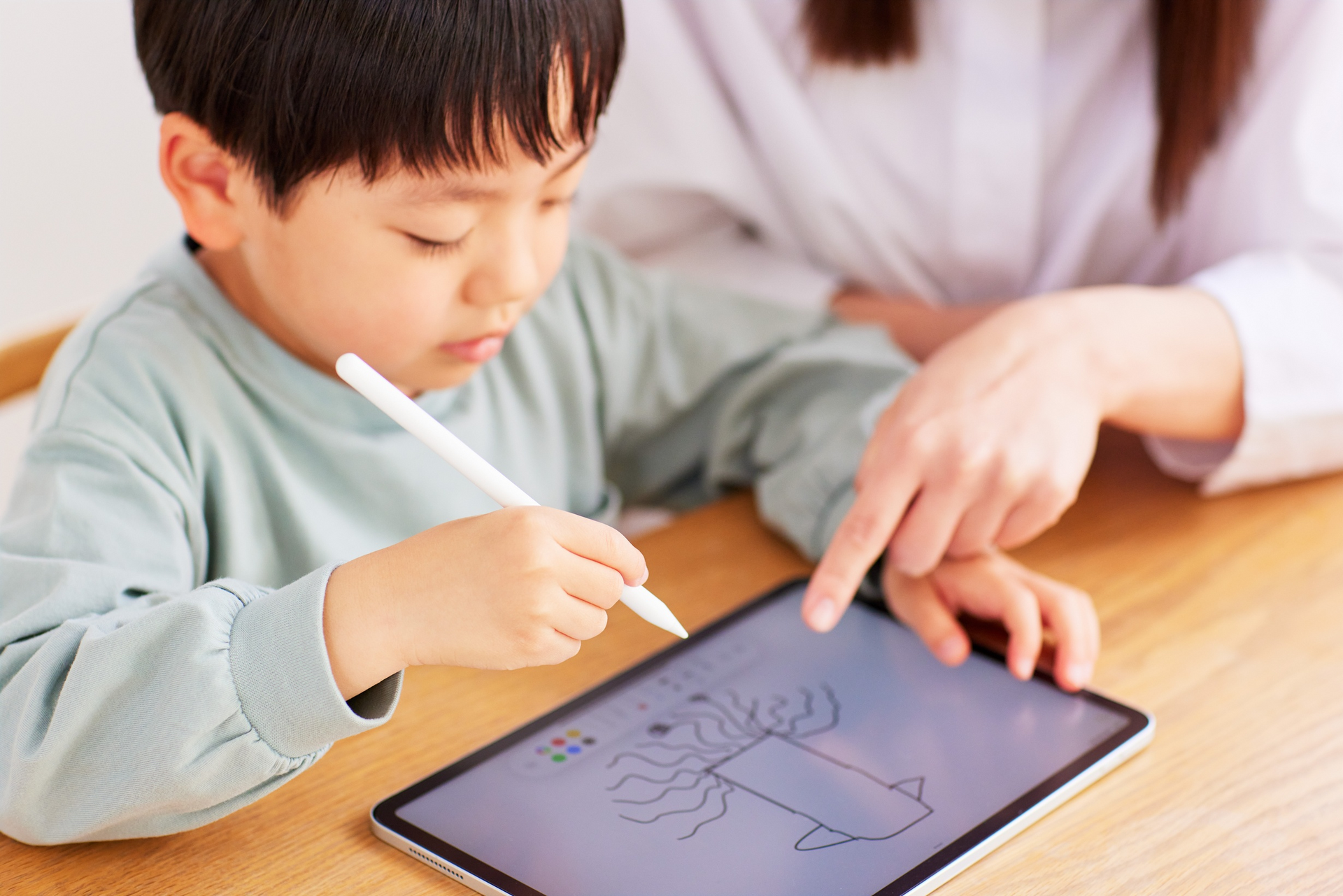 A woman is teaching a young boy how to use a tablet computer.