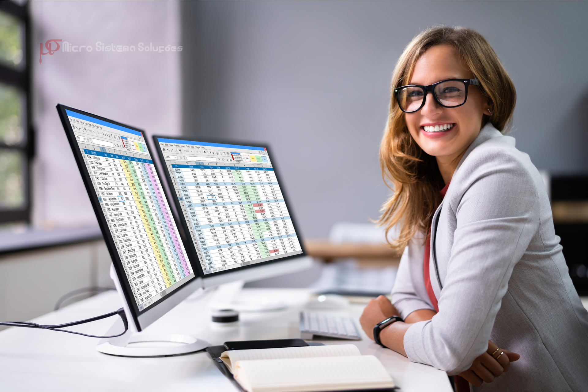 A woman is sitting at a desk in front of two computer monitors.