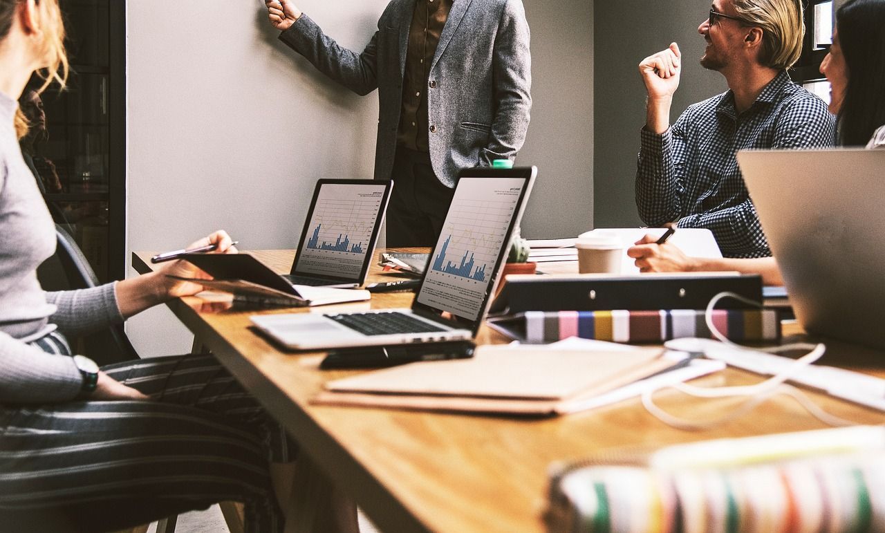 Um grupo de pessoas está sentado ao redor de uma mesa com laptops.