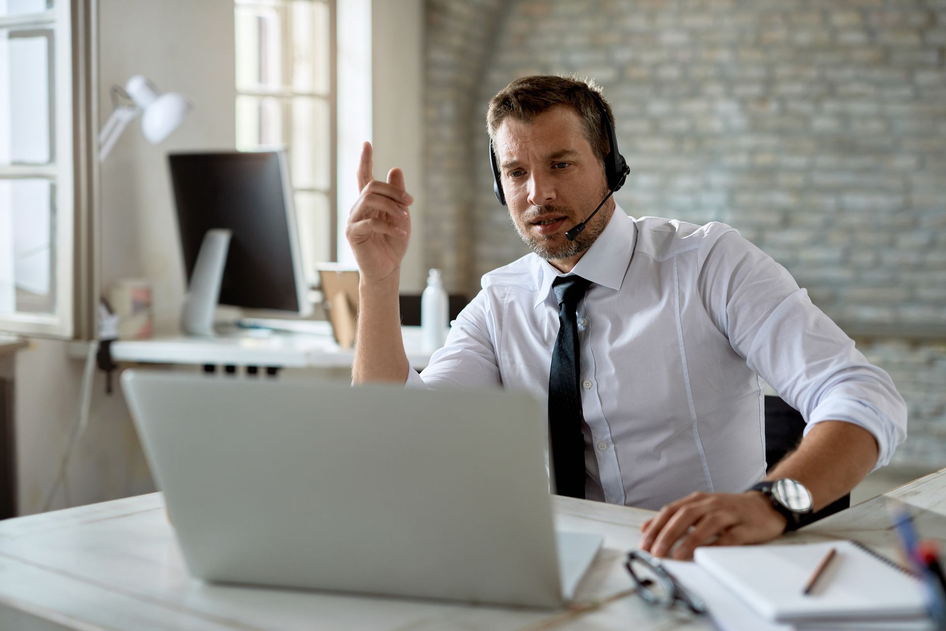 A man wearing a headset is sitting at a desk in front of a laptop computer.