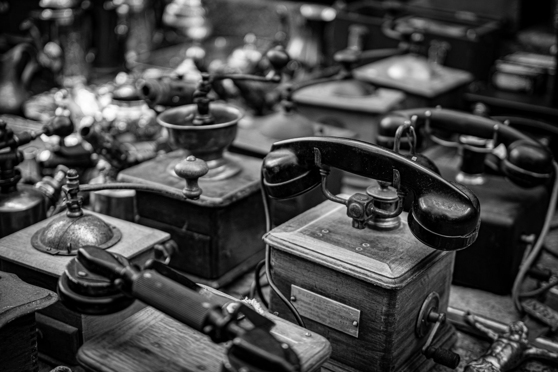 Imagem em close-up de telefones antigos e outros dispositivos antigos dispostos sobre uma superfície, em preto e branco.