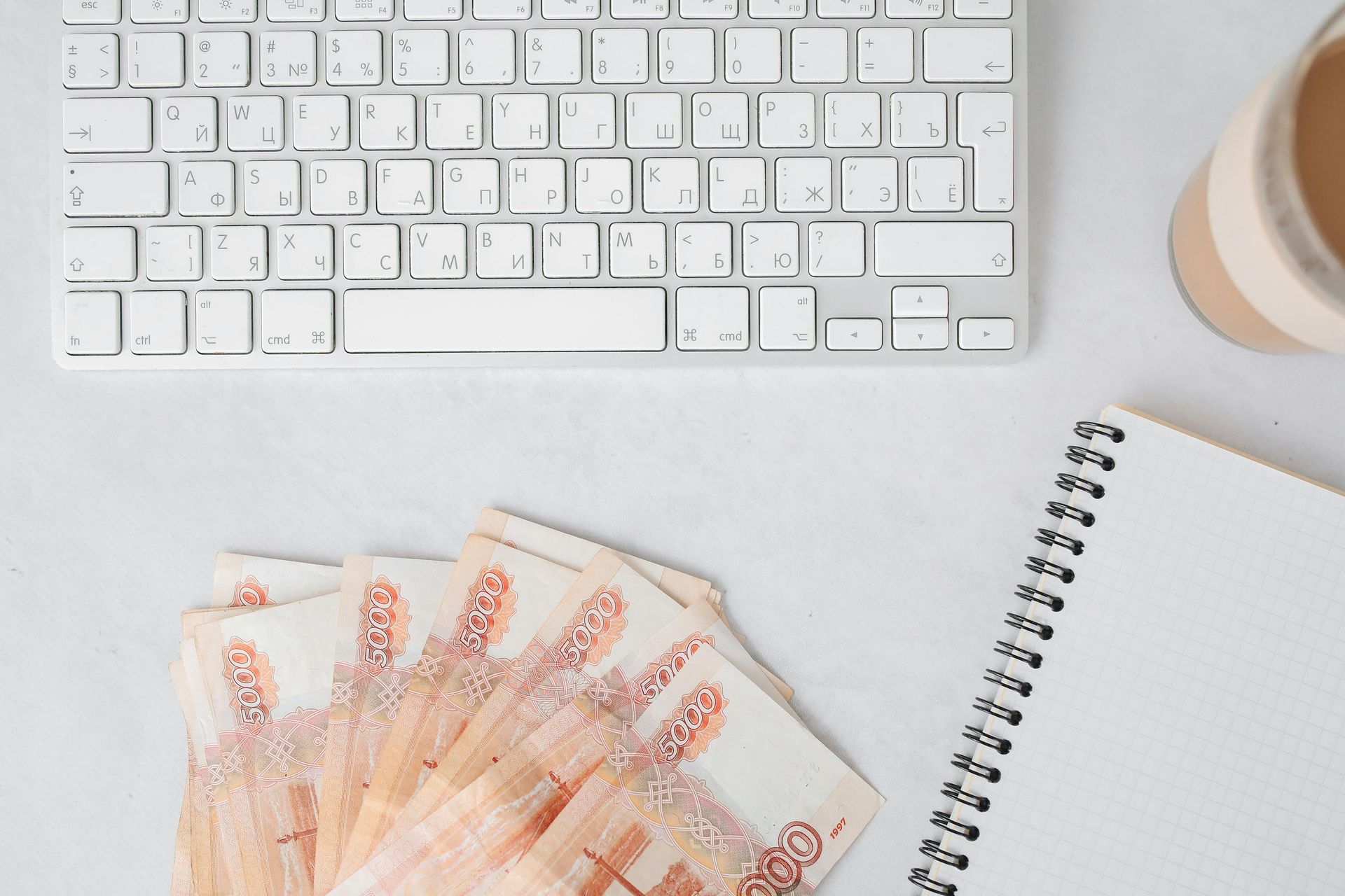 A bunch of money is sitting next to a keyboard and a cup of coffee.