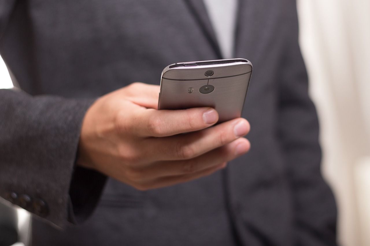 A man in a suit is holding a cell phone in his hand.